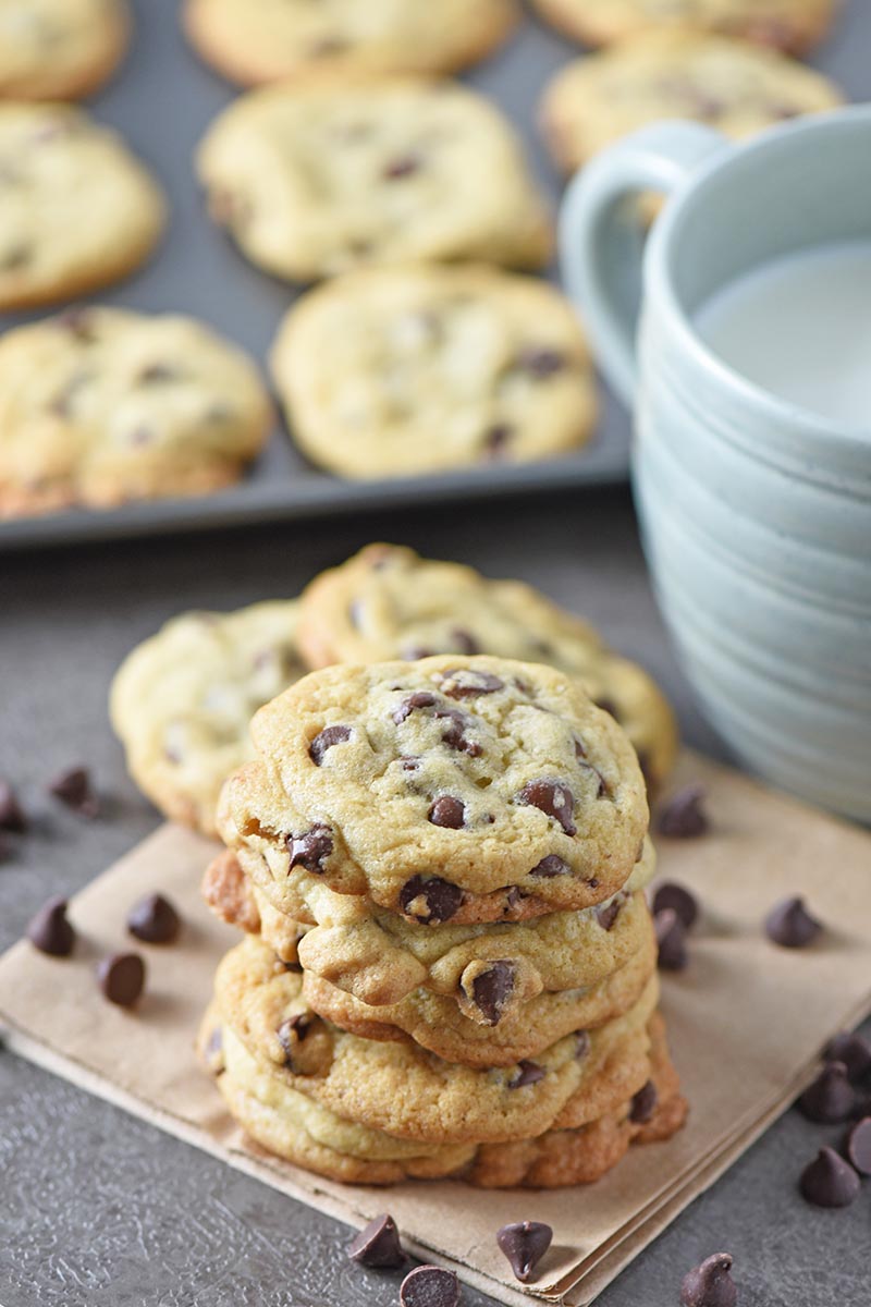 stack of easy chocolate chip cookies on brown paper bag with light blue mug of milk