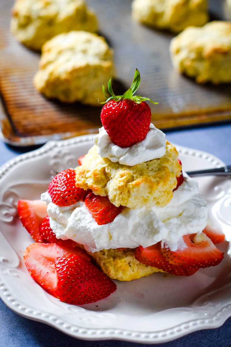 easy strawberry shortcake recipe with biscuit sliced in half and topped with whipped cream and fresh strawberries on white plate with fork
