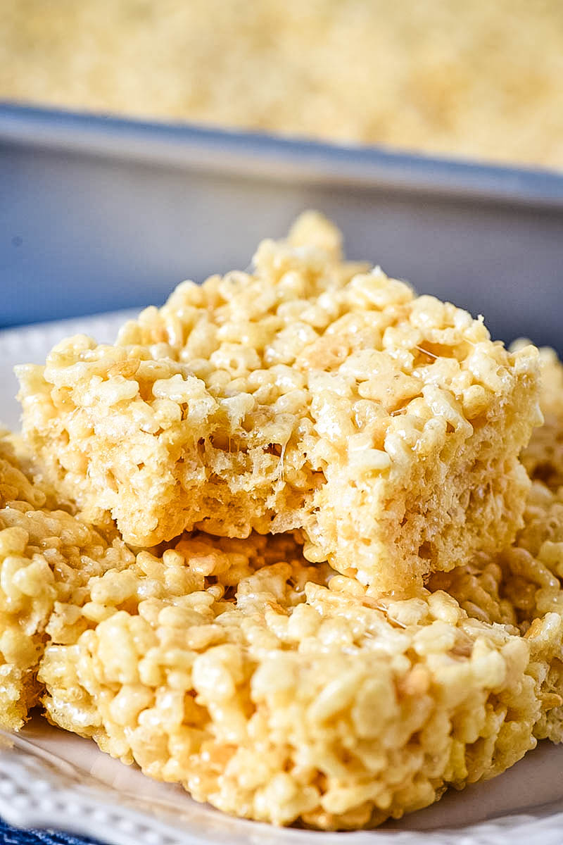 pile of Rice Krispie squares on white plate with bite taken out of one Rice Krispie treat