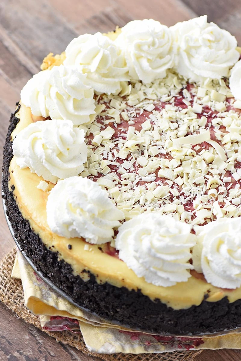 white chocolate raspberry cheesecake with whipped cream swirls on wood countertop