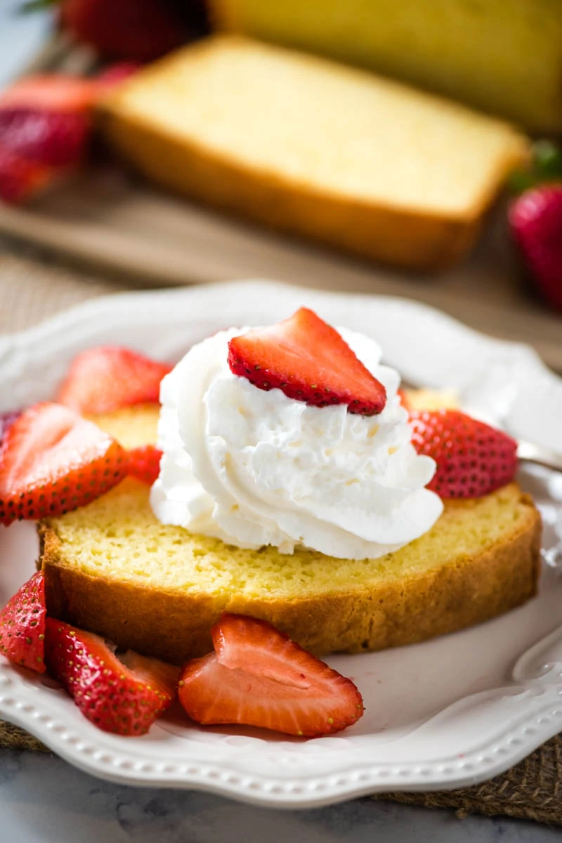 moist pound cake topped with whipped cream and fresh strawberries on white plate
