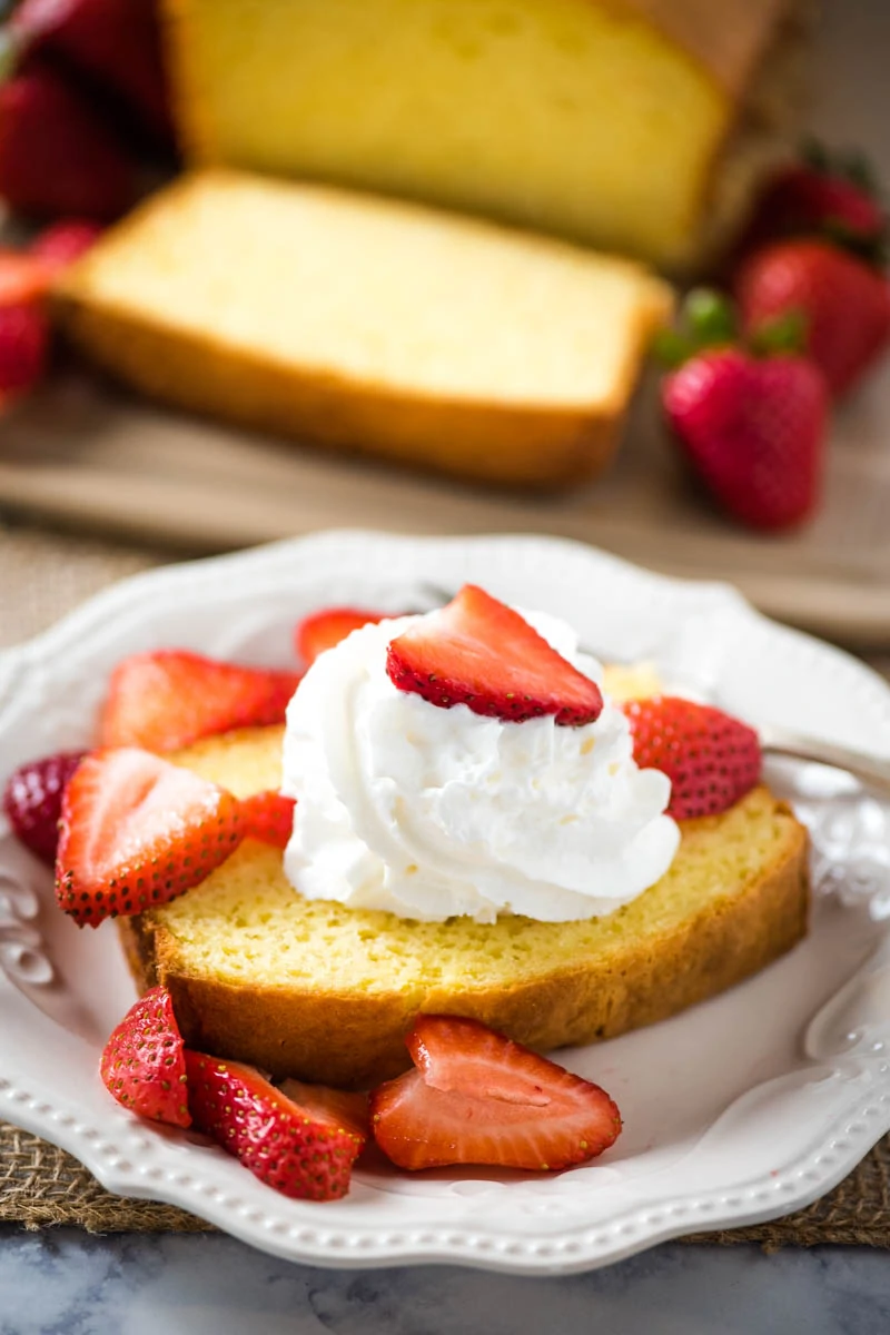 sliced pound cake with whipped cream and strawberries on white plate