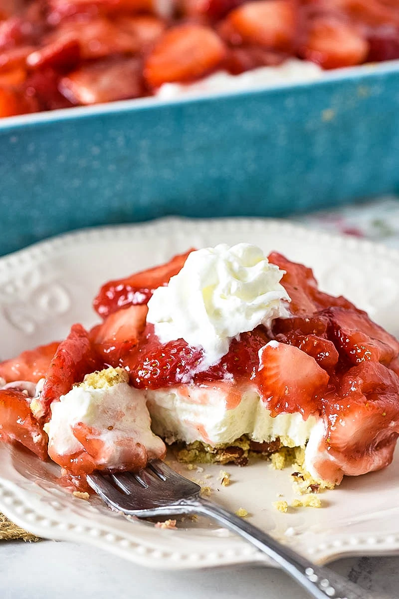 slice of no bake strawberry dessert with whipped cream and bite on white plate with fork