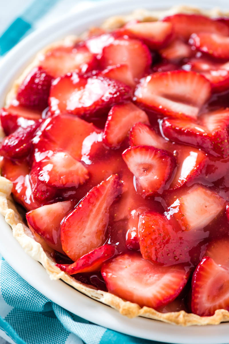fresh strawberry pie in white pie plate with teal checkered kitchen napkin