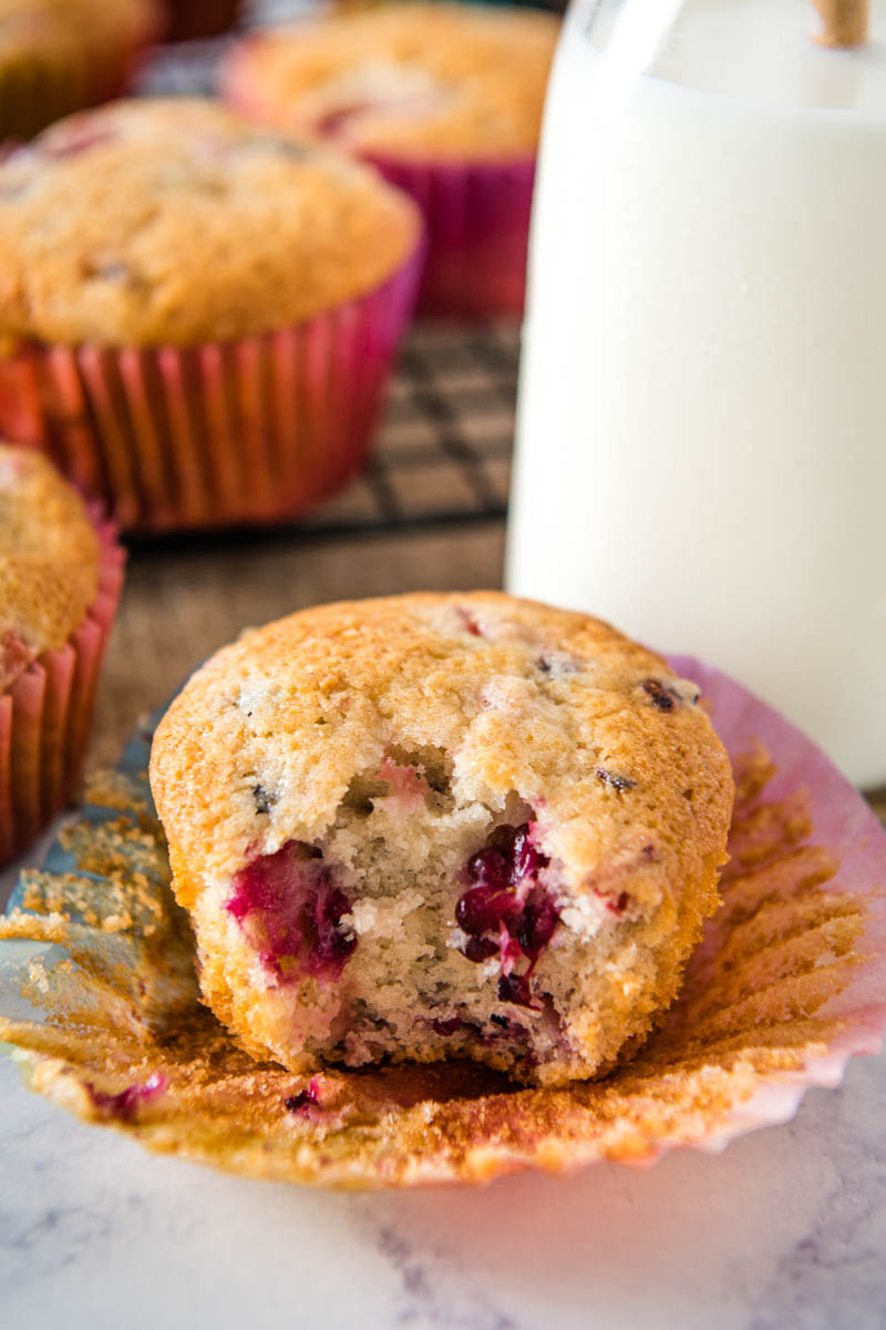 bite out of strawberry blackberry muffin on cupcake liner with glass of milk