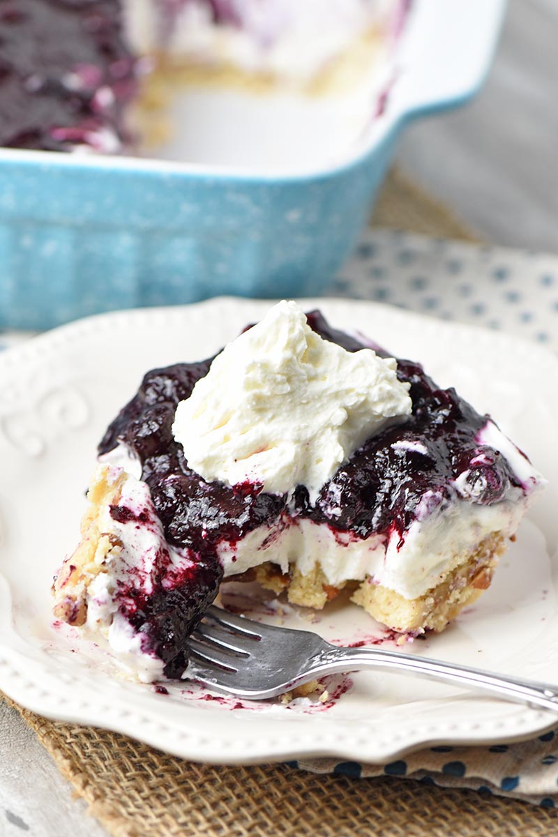 slice of no bake blueberry dessert with whipped cream on top sitting on white plate and bite on fork