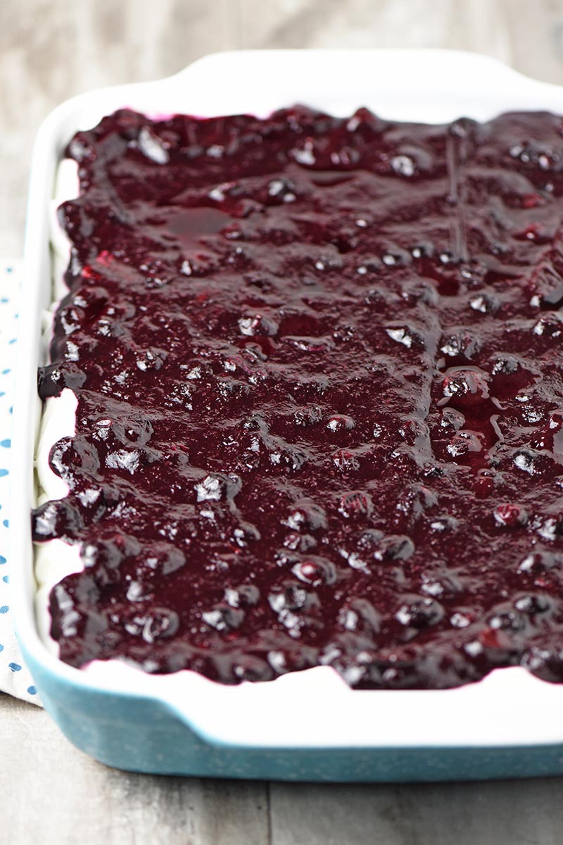 blueberry pie filling over cream cheese filling in blue baking dish