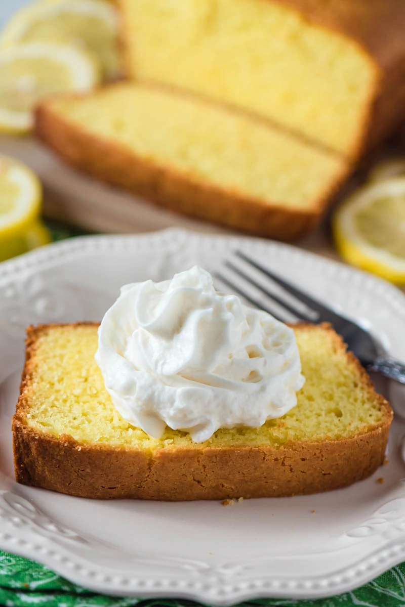 sliced lemon pound cake with dollop of whipped cream on white plate with fork
