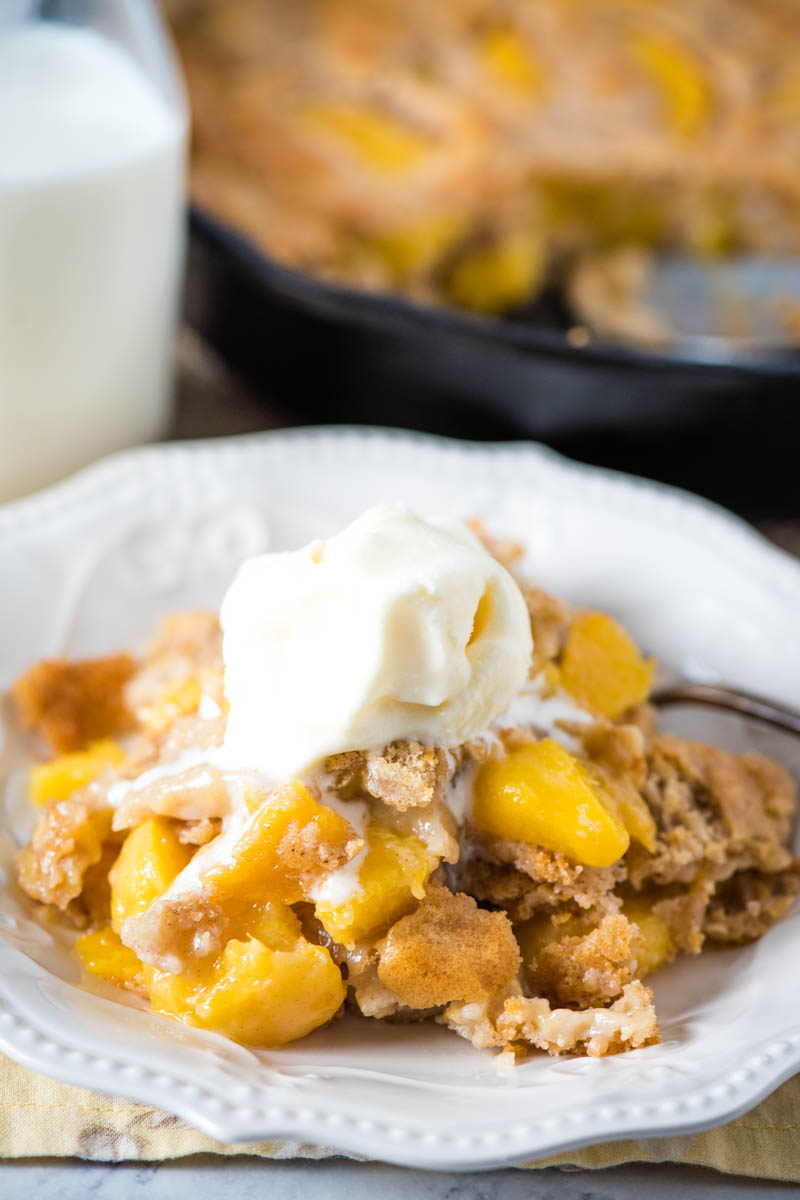 serving of Bisquick peach cobbler on white plate with fork and vanilla ice cream