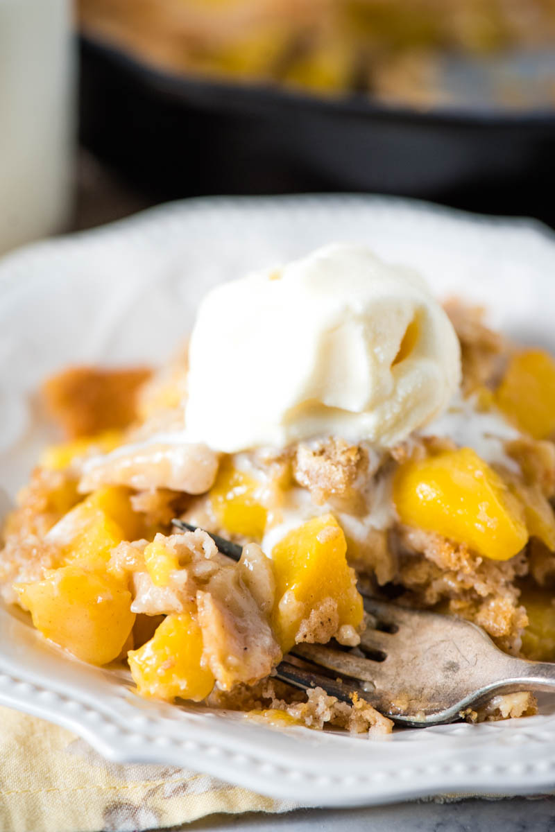 fork full of old-fashioned peach cobbler on white plate with scoop of vanilla ice cream
