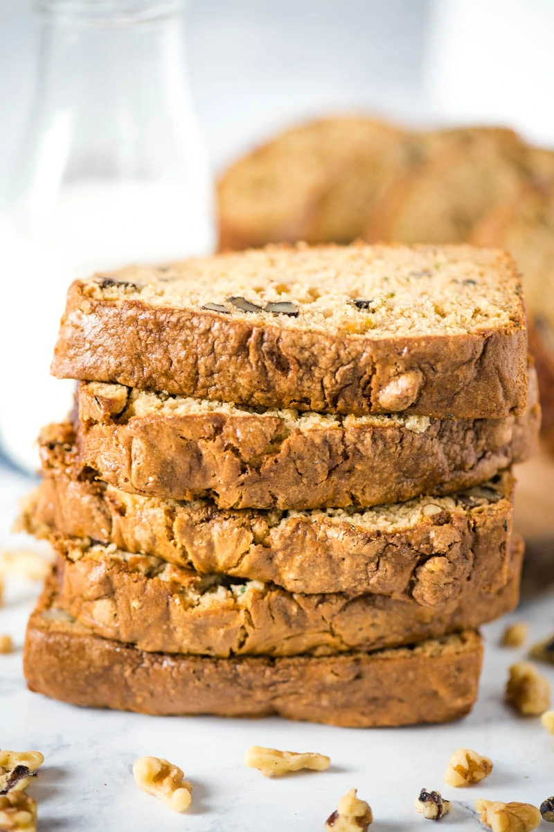 stacked slices of gluten-free zucchini bread with walnuts and glass of milk on white marble countertop