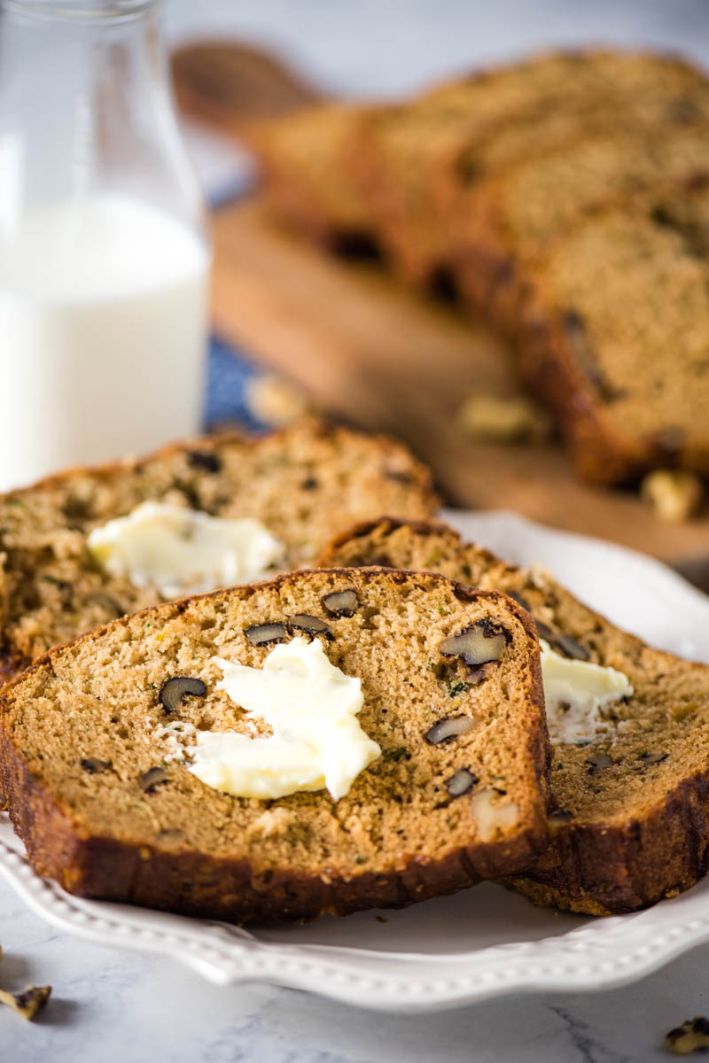 buttered slices of zucchini nut bread on white plate with glass of milk