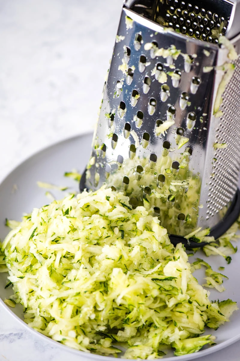 grated zucchini with grater on gray plate