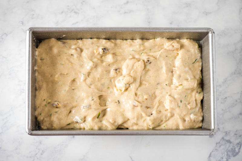 zucchini bread batter in metal loaf pan on white marble countertop
