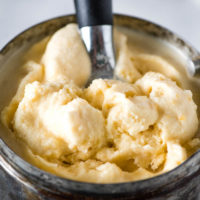 scooping peach ice cream out of metal ice cream maker canister with ice cream scoop