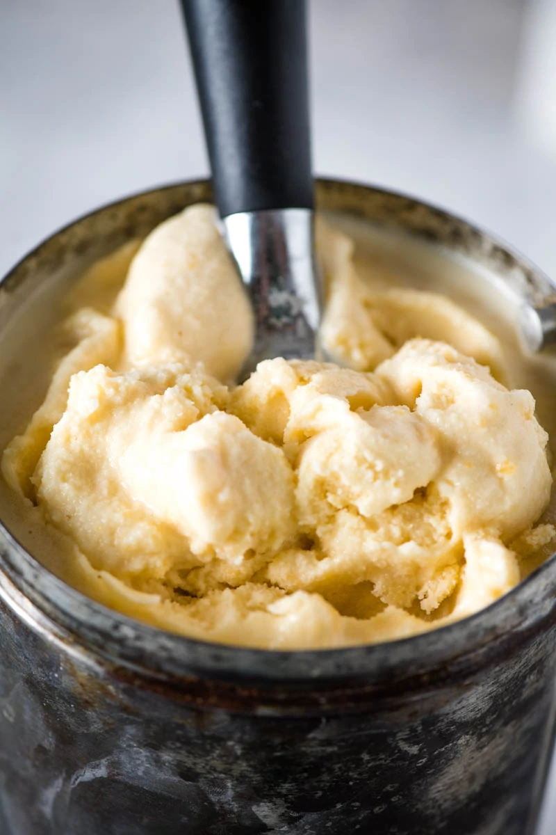 scooping peach ice cream out of metal ice cream maker canister with ice cream scoop