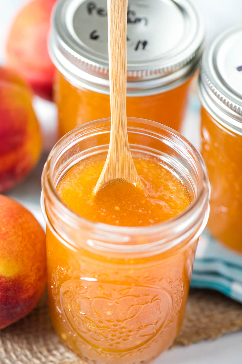 jar of homemade peach jam with small wooden spoon