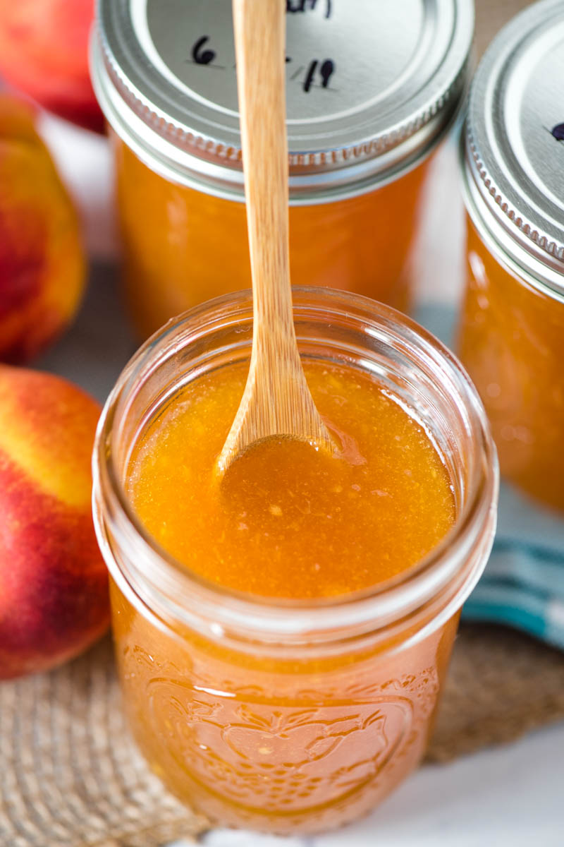 peach jam in jar with wooden spoon in it
