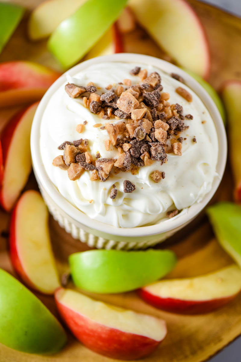 white ramekin filled with caramel cream cheese dip with toffee bits on top and served with apple slices