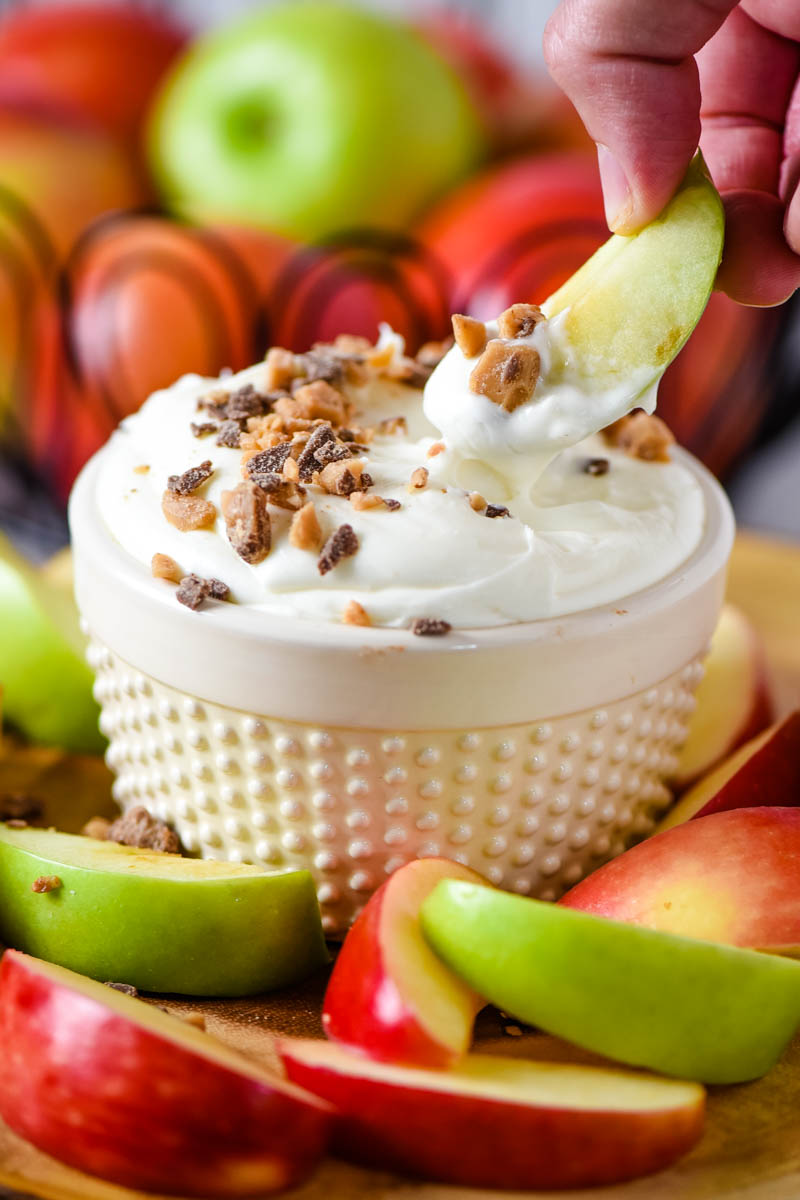 dipping Granny Smith apple slice in ramekin full of cream cheese caramel apple dip with chocolate toffee bits on top