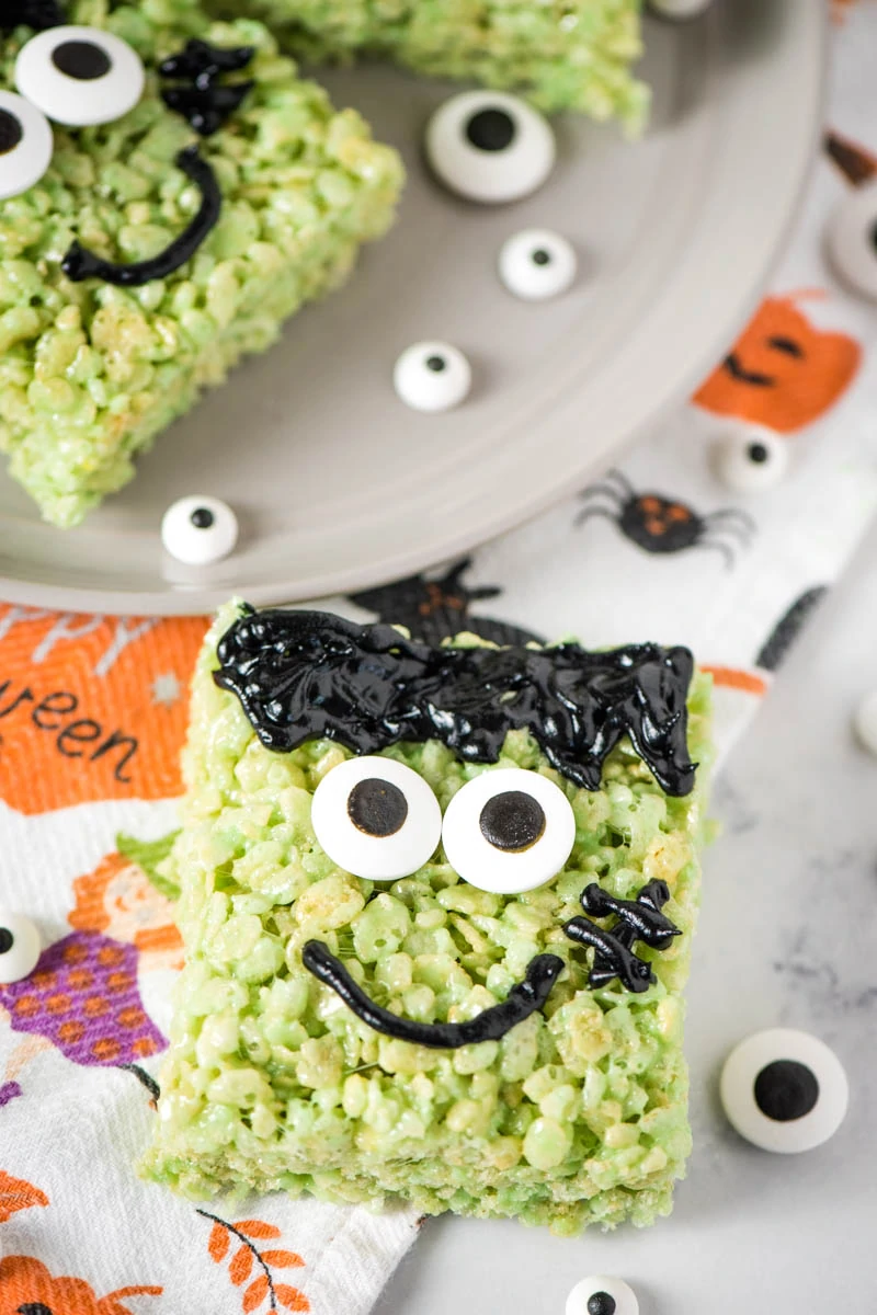 Frankenstein marshmallow treats with candy eyes on white marble countertop with Halloween dish towel