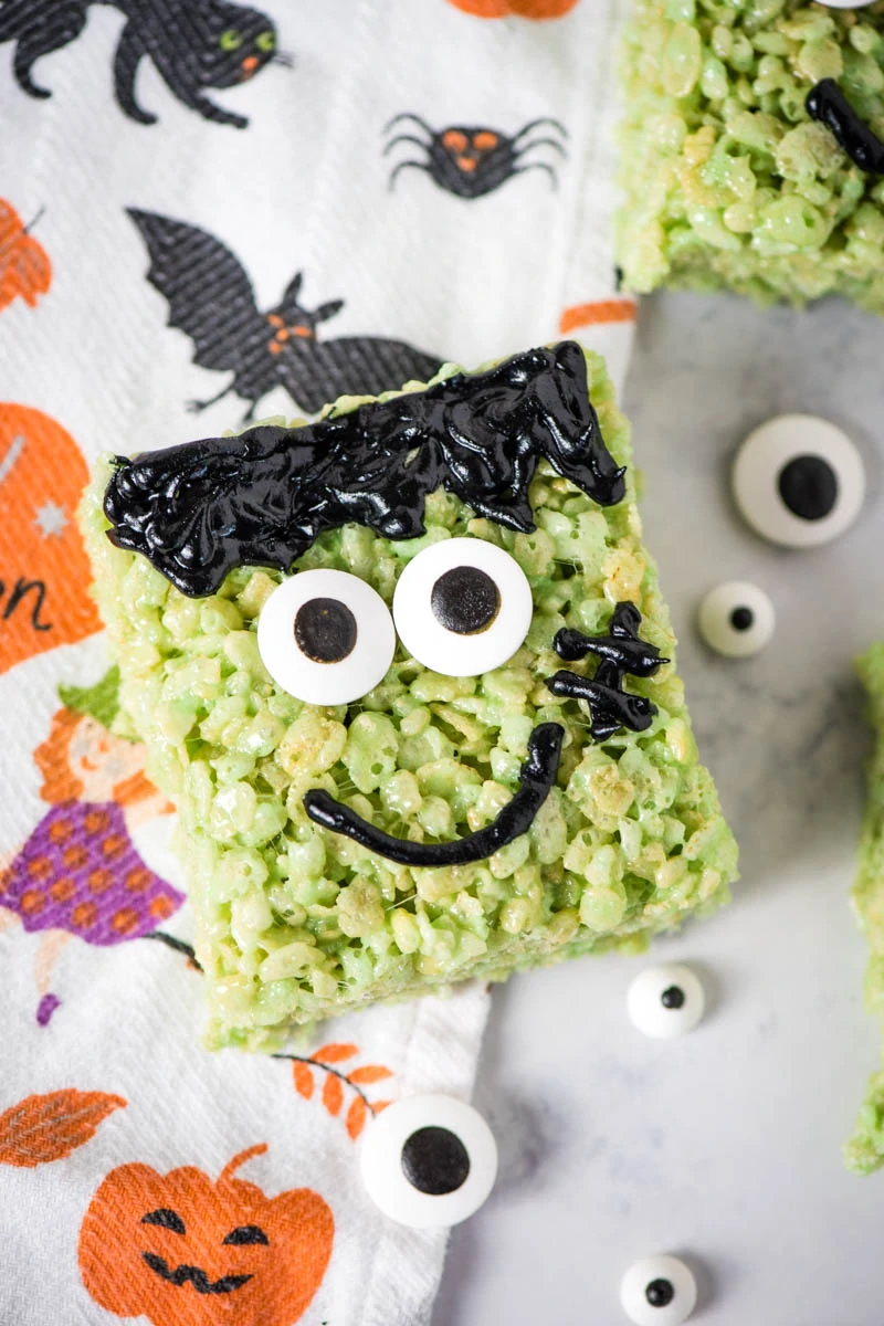 Frankenstein Rice Krispie treats on white marble countertop with candy eyes and Halloween dish towel