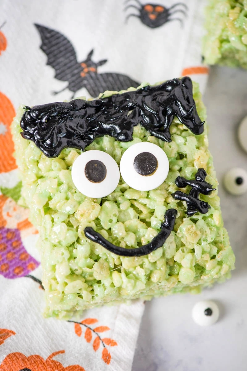 green Halloween cereal treats decorated like Frankenstein on white marble countertop with Halloween dish towel