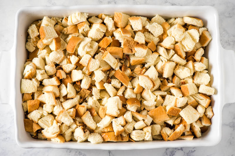 layering bread cubes and pecans in white casserole dish for sweet breakfast casserole