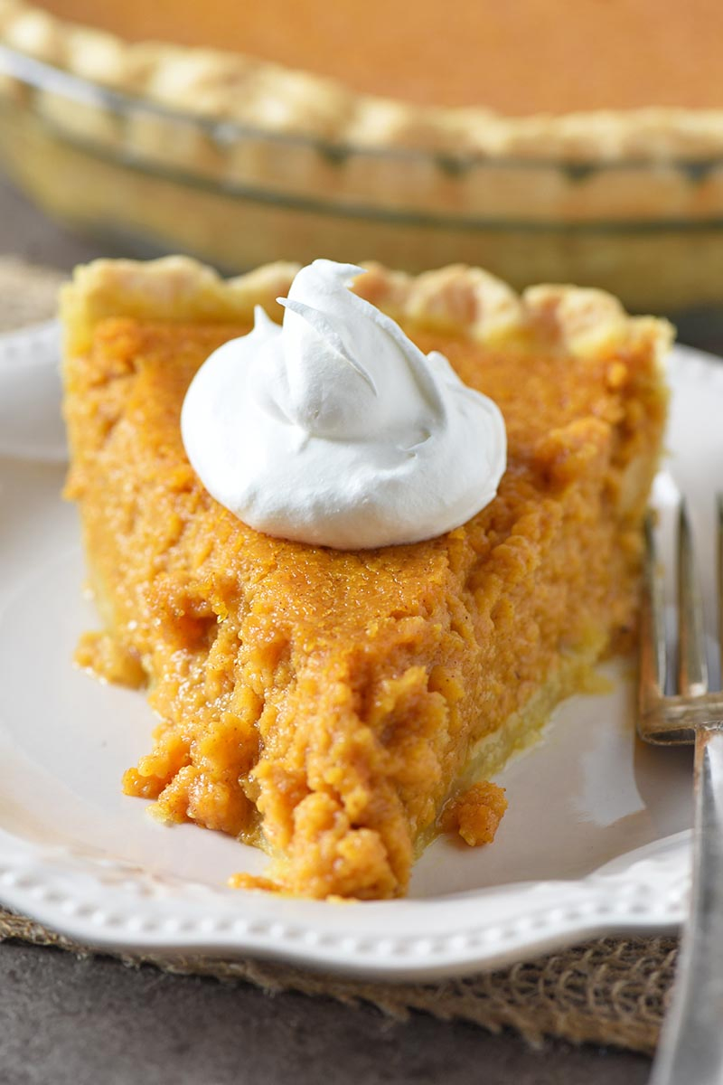 slice of southern sweet potato pie with whipped cream topping and fork on ivory colored plate
