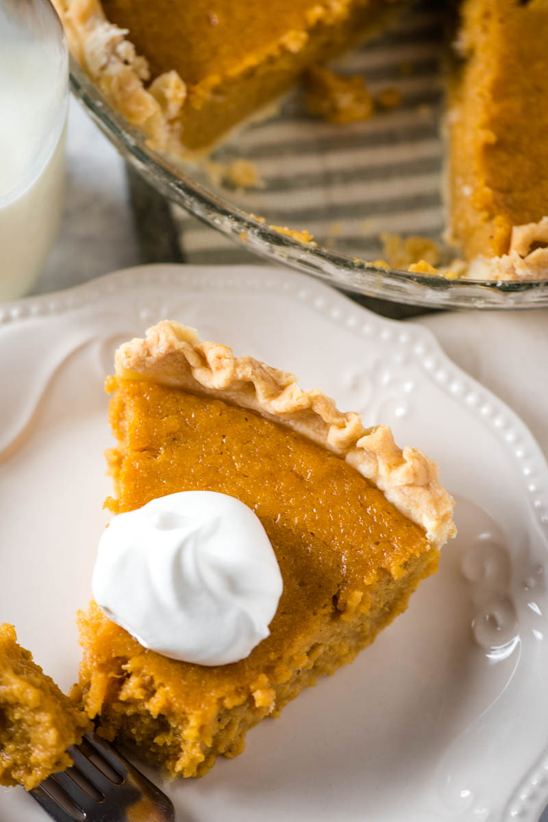 slice of sweet potato pie recipe on white plate with full pie and glass of milk