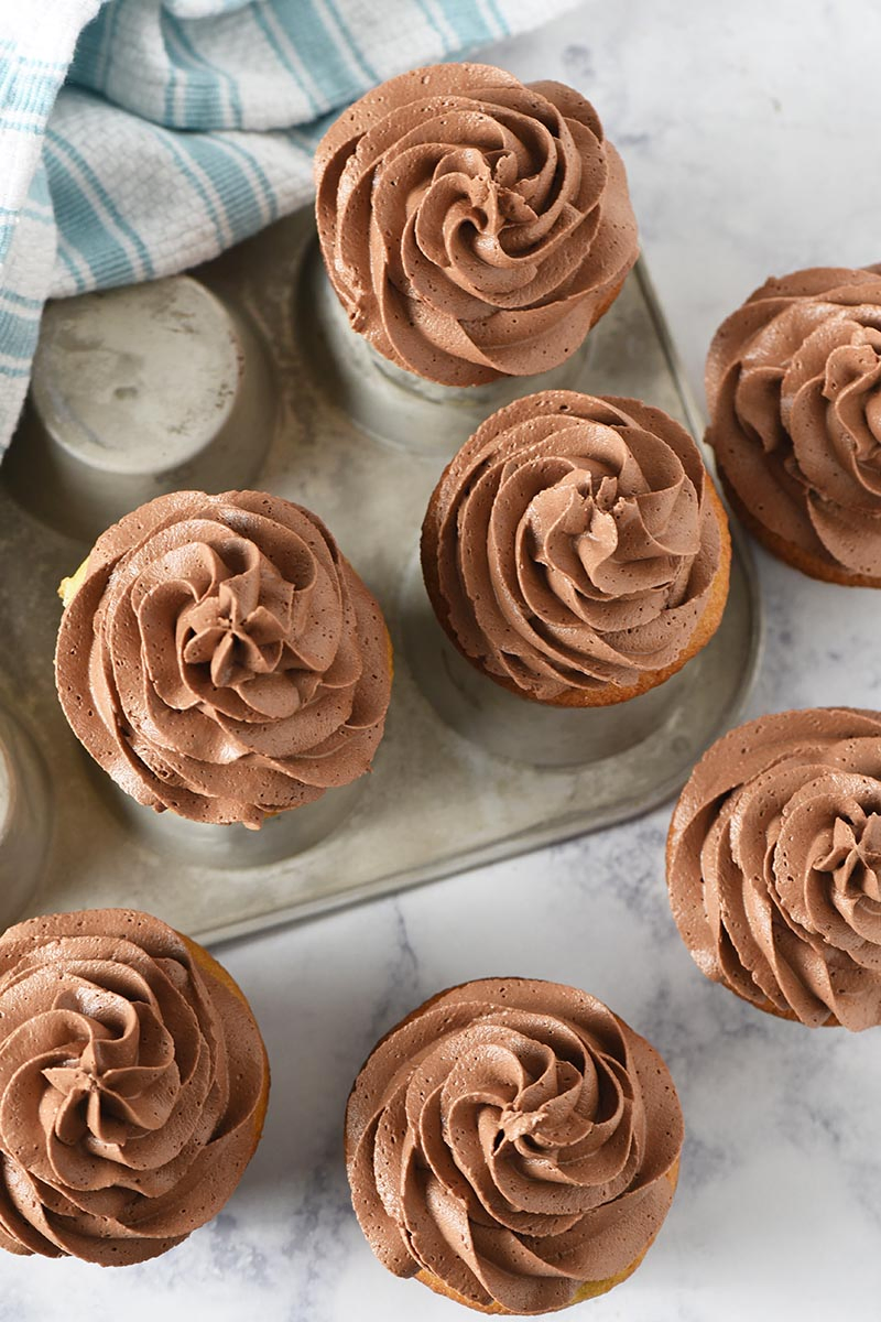 swirls of homemade chocolate buttercream with cocoa powder on cupcakes