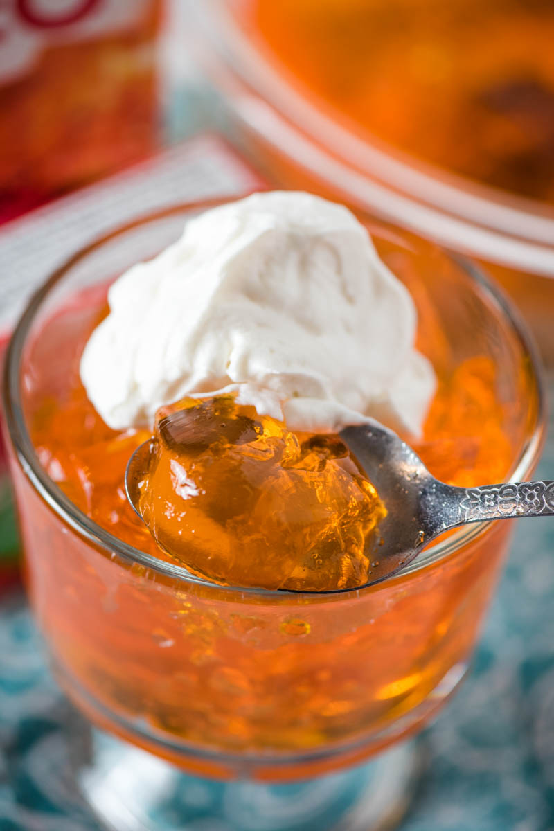 bite of orange Jello with Dream Whip whipped cream on spoon in glass mini trifle dish