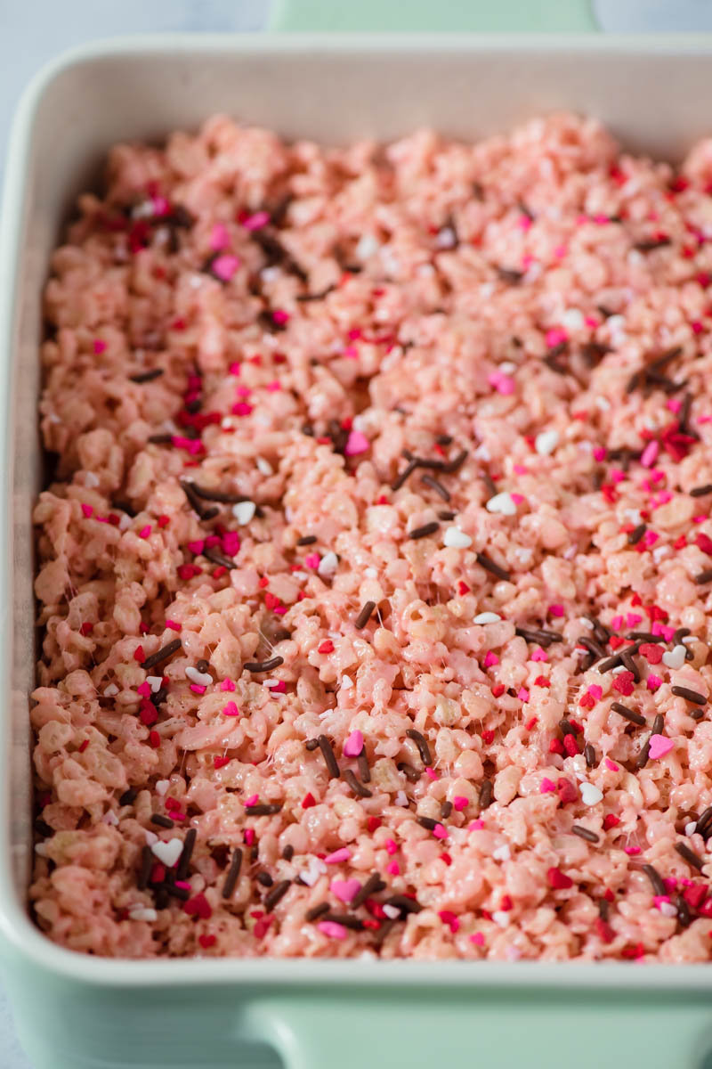 spreading pink rice crispy treats in mint green baking dish with Valentine heart sprinkles on top