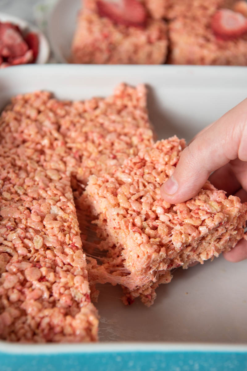 pulling sliced strawberry Rice Krispies treat out of blue baking pan