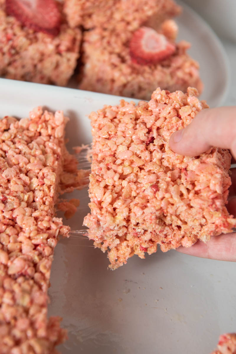 pulling strawberry marshmallow Rice Krispie treat out of white baking dish