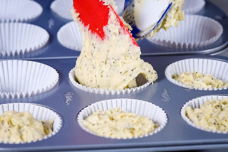 scooping lemon poppy seed muffin batter into lined muffin tin with spatula and batter spoon