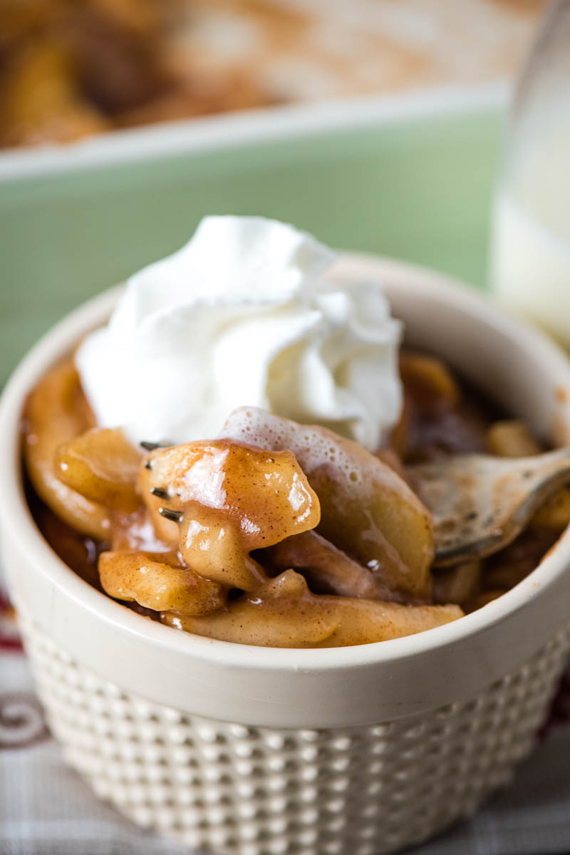 forkful of baked apples with cinnamon and whipped topping in ivory ramekin