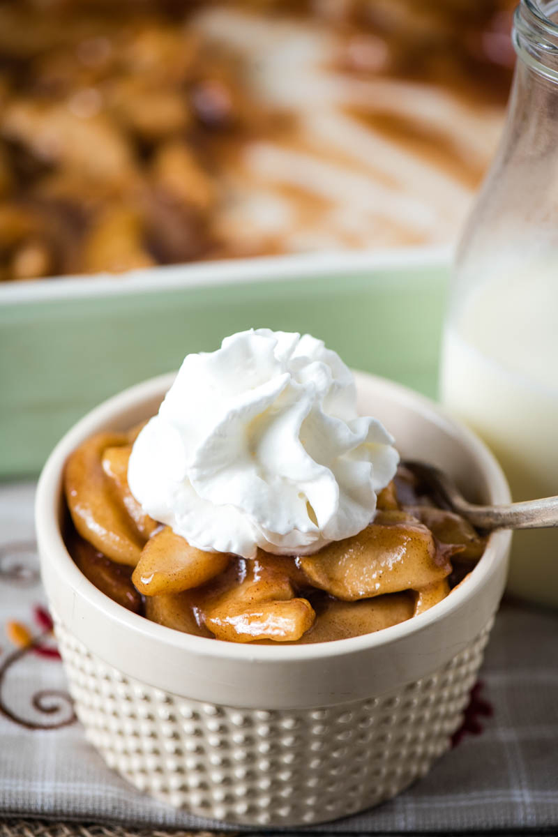 baked apples with whipped cream on top in ivory ramekin with fork