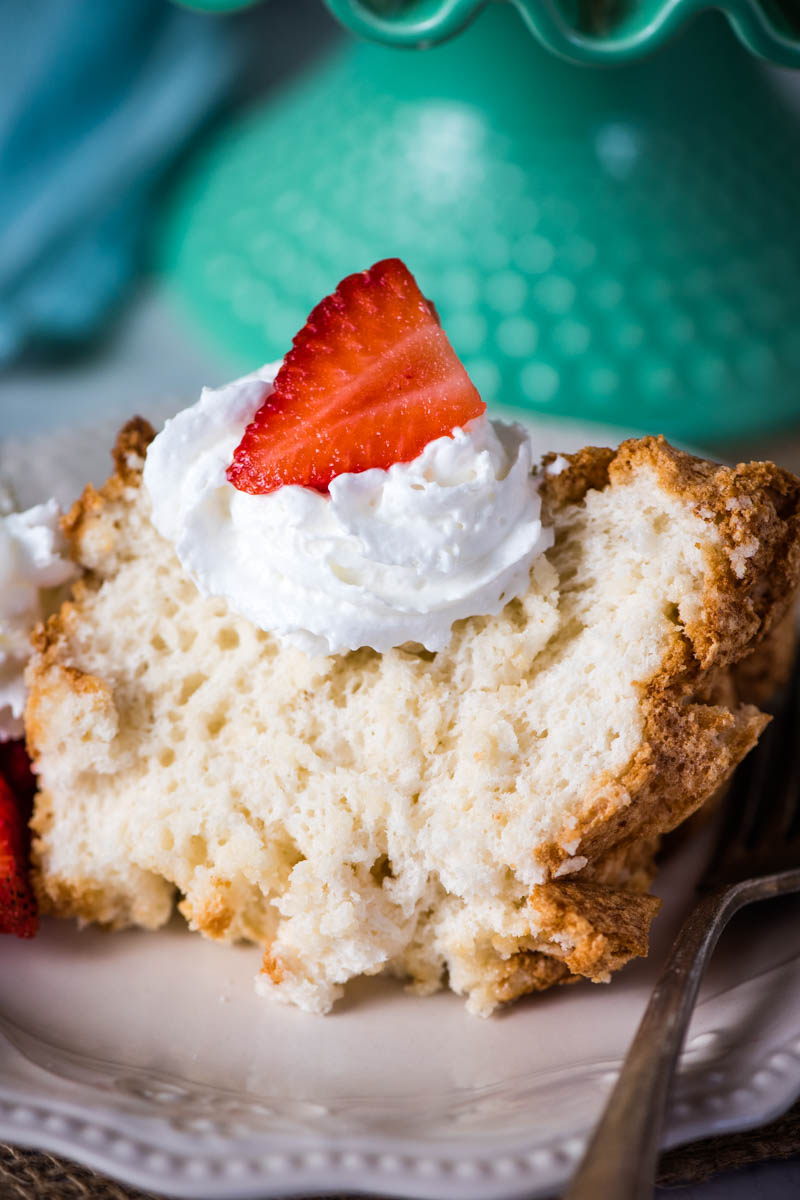 slice of homemade angel food cake with strawberries and whipped cream on white plate with fork