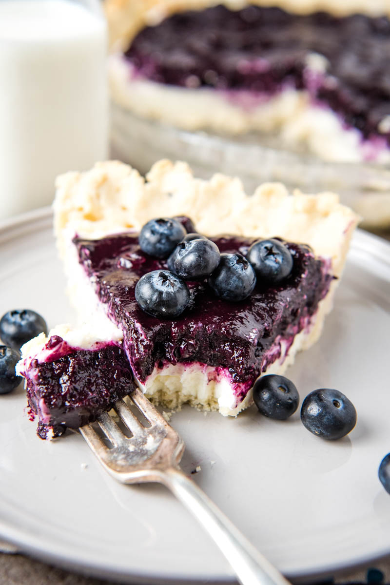 slice of blueberry cream cheese pie on gray plate with bite on fork and fresh blueberries