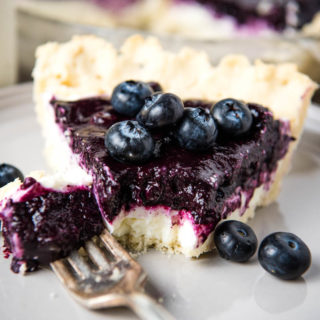 slice of cream cheese blueberry pie with blueberries on top and bite taken out of pie on gray plate with fork and bite