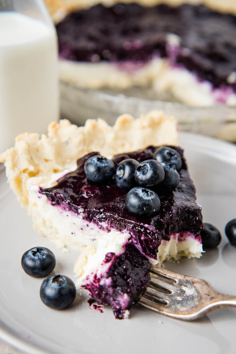bite out of creamy blueberry pie slice on gray plate with fork and fresh blueberries