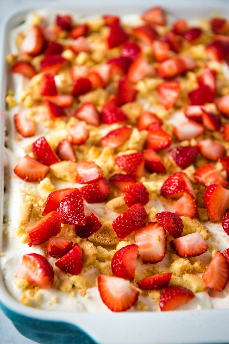 no bake strawberry shortcake topped with fresh strawberry chunks and crushed vanilla wafers in blue baking dish