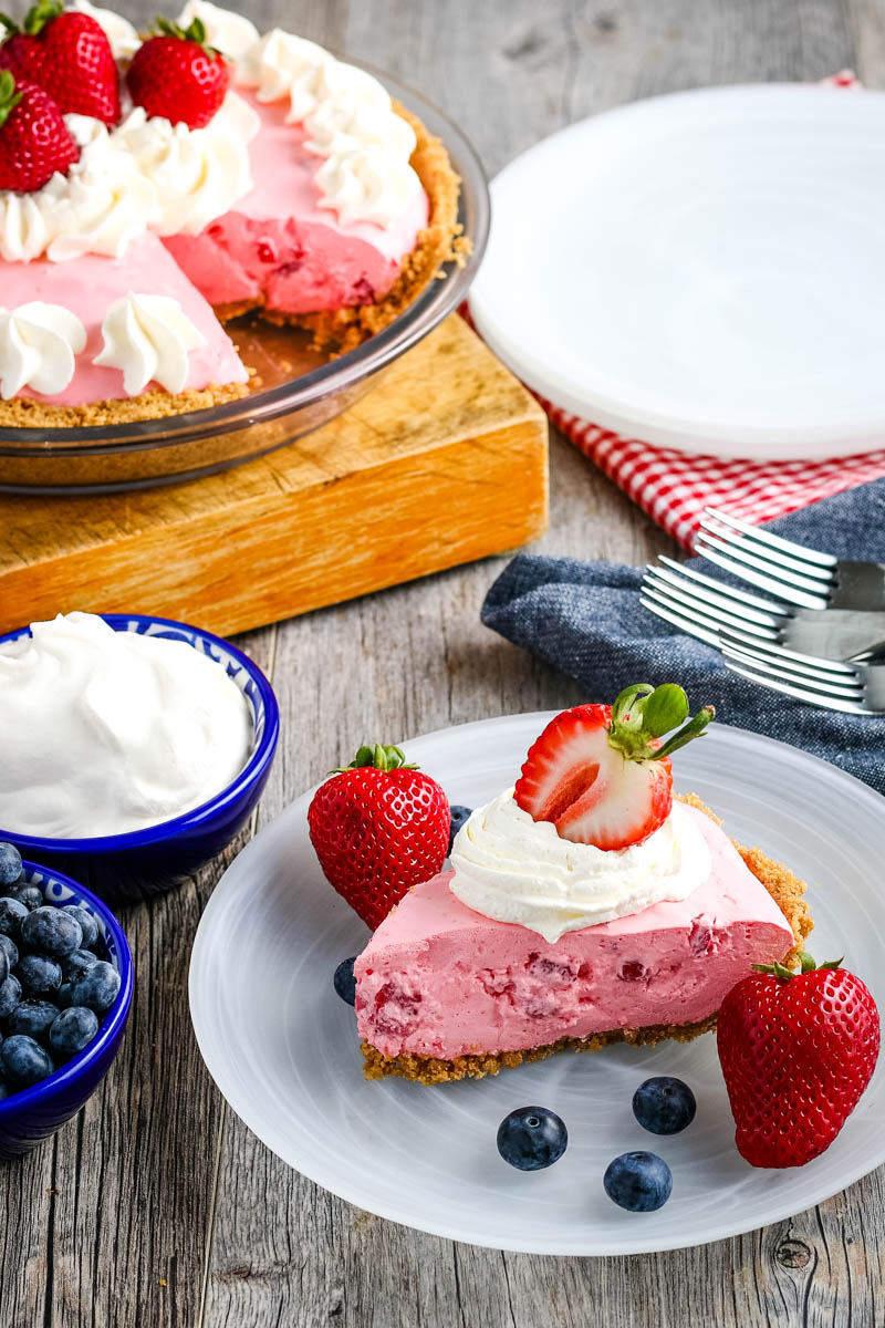 sliced strawberry fluff pie on clear plate, on wooden countertop, topped with Cool Whip and fresh berries