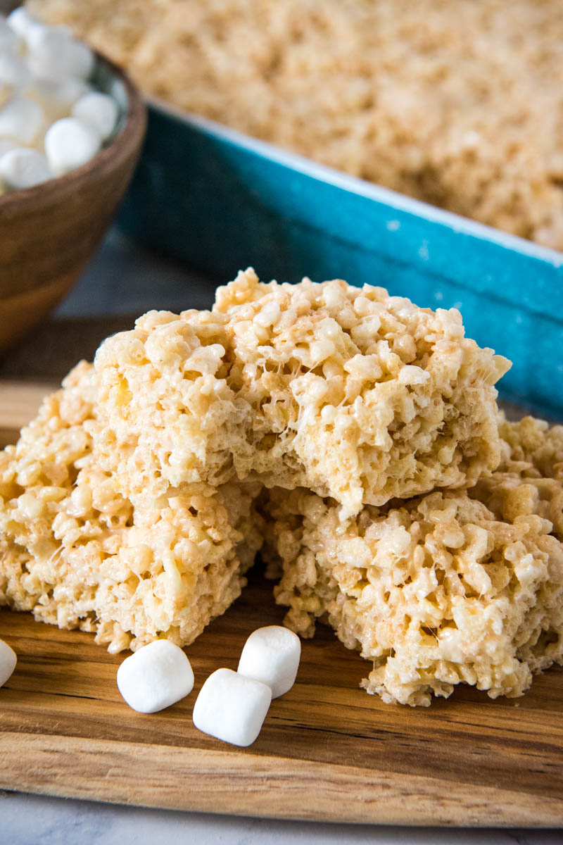 stack of microwave Rice Krispie treats with bite taken out on wooden cutting board with mini marshmallows