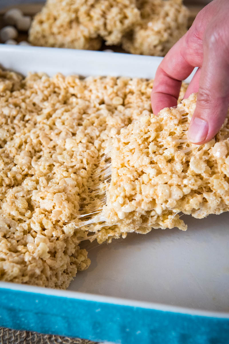 hand pulling microwave Rice Krispies treats out of turquoise and white baking dish