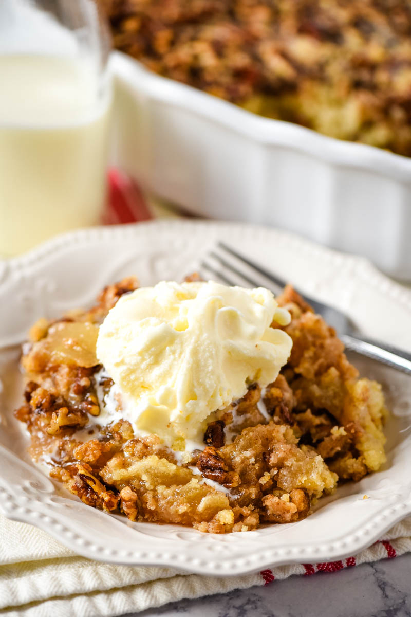 scoop of caramel apple pecan dump cake with vanilla ice cream on white plate with fork