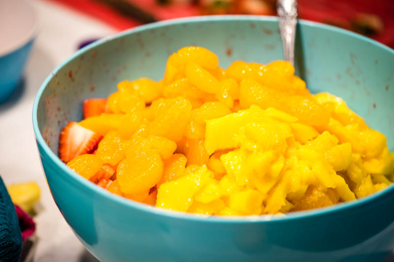 mandarin oranges and fresh mango added to blue mixing bowl for tropical fruit salad