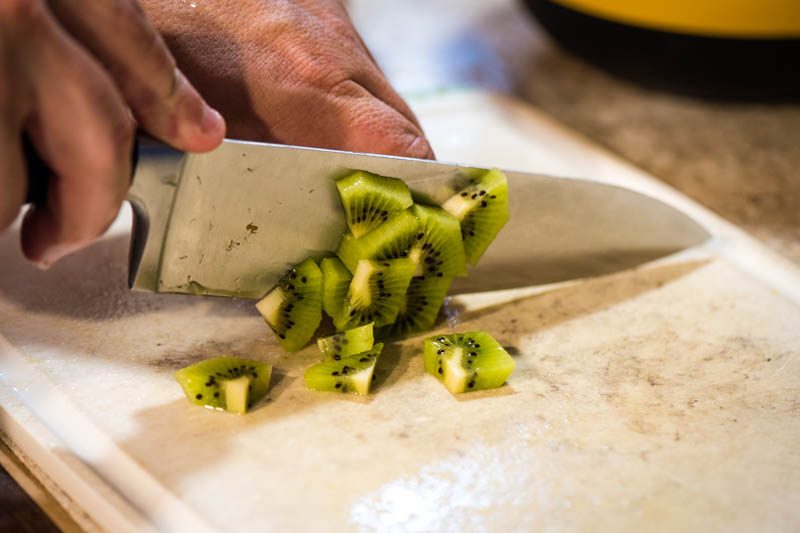 chopping kiwi for fruit salad on white cutting board