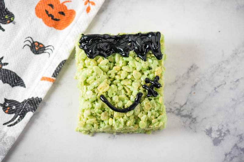 decorated green Rice Krispie treats with black icing for Frankenstein hair, smile, and stitches